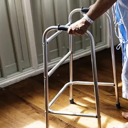Persona mayor usando un andador estándar en una habitación de hospital.